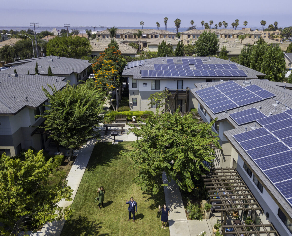 Aerial view of modern homes with solar panels on roofs in a suburban neighborhood with green trees and landscaping