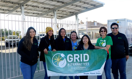 Seven people holding a green GRID Alternatives banner at an outdoor event