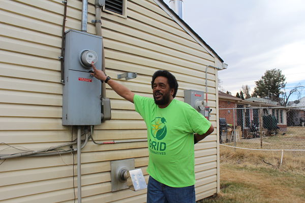 Gary, wearing his green GRID t-shirt, points to his electric meter and explains how he has been saving money with his solar system