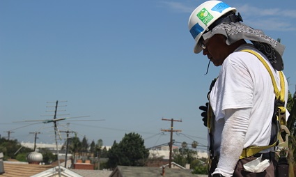 Construction worker in safety helmet and harness on rooftop surveying job site