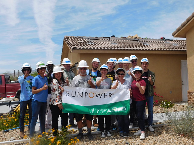 Group of construction workers in hard hats holding Sunpower banner at residential home installation site