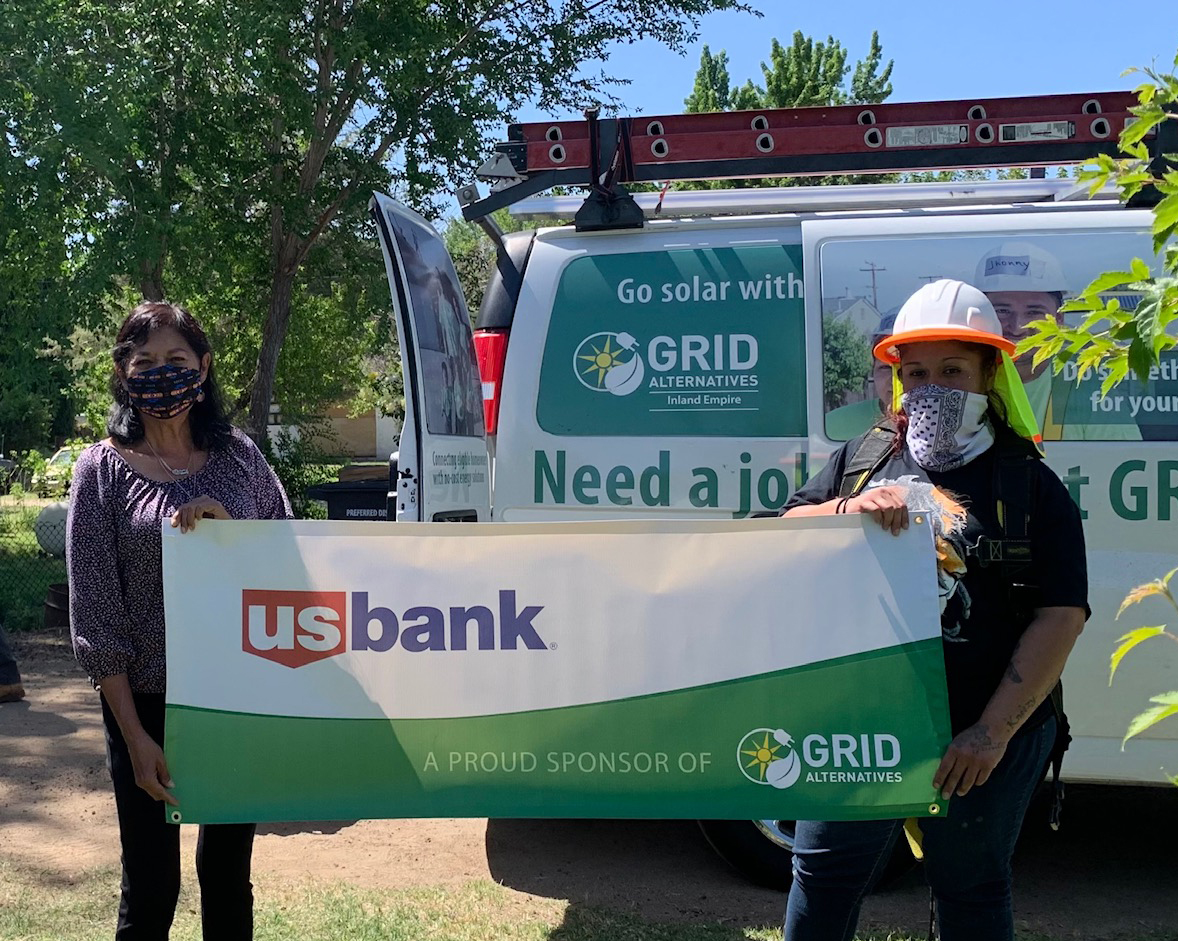 Two people holding US Bank banner in front of GRID Alternatives solar van