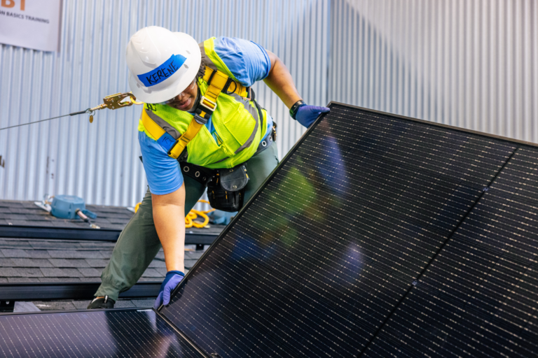 Worker installing solar panel on roof wearing safety harness and hard hat