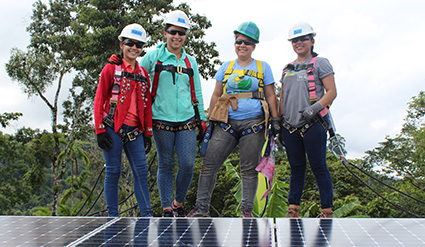Four workers in safety gear stand on a solar panel installation outdoors
