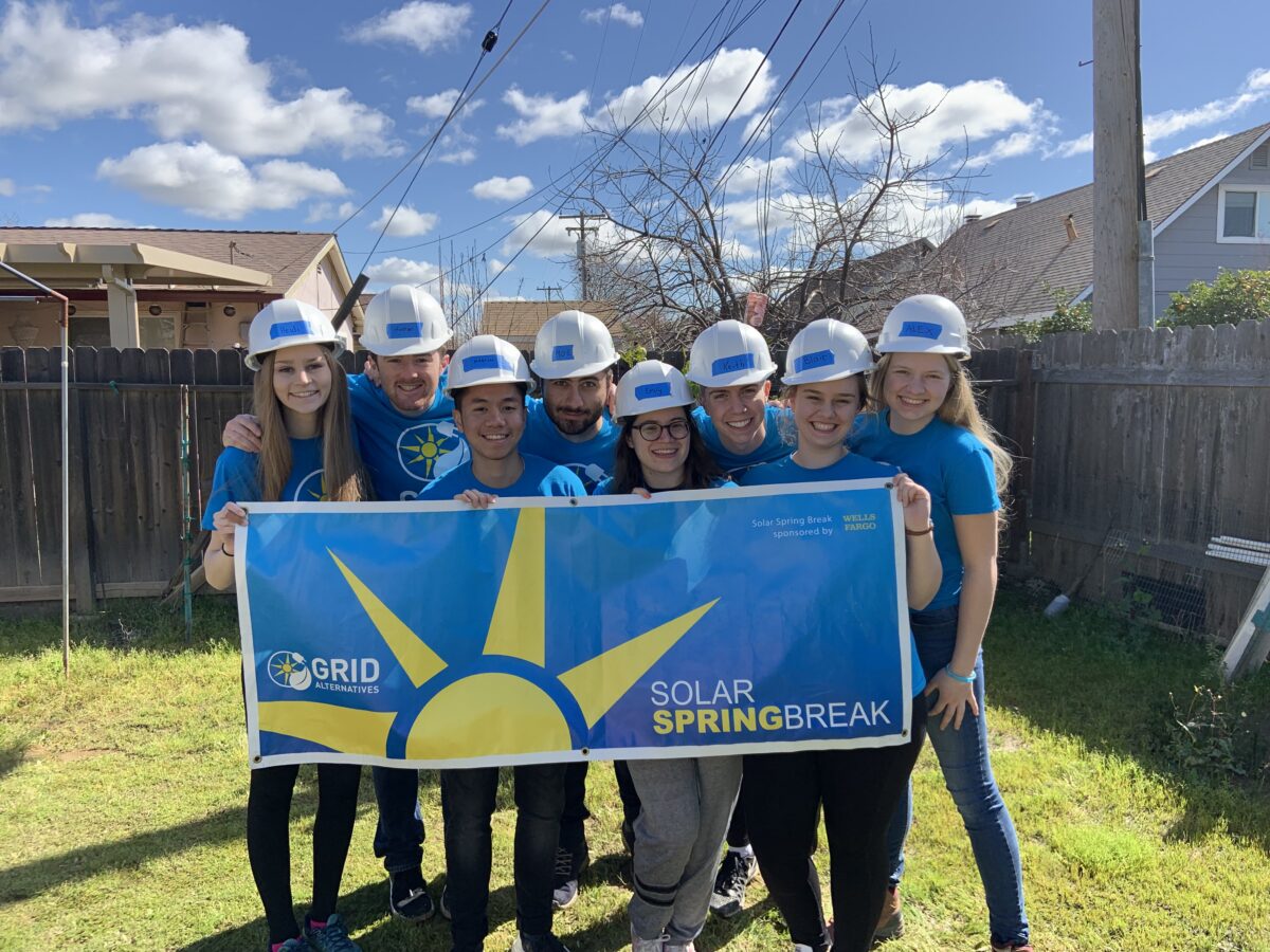 Team in hard hats holding Solar Springbreak banner in residential backyard