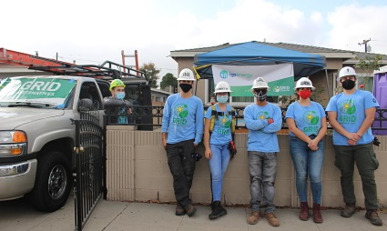 Six volunteers in blue shirts and hard hats stand in front of a work truck and blue-roofed structure