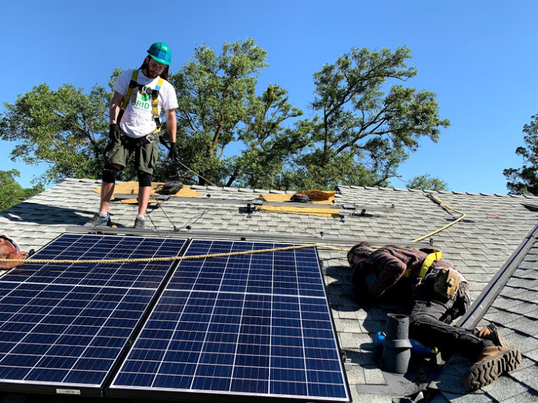 Two workers installing solar panels on a residential roof under clear blue sky