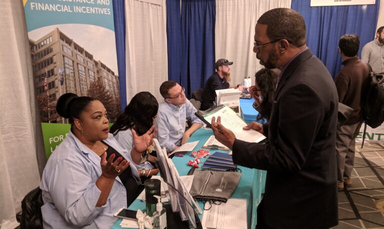 Man in business attire speaking with female staff at a booth about real estate finance and financial incentives