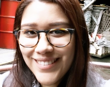 Person with long brown hair wearing glasses and smiling at camera indoors