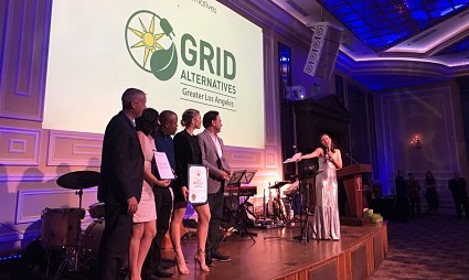 Panel discussion at GRID Alternative conference with five speakers on stage and blue stage lighting