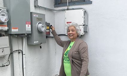 Woman pointing at electrical meter panel on white wall, wearing green lanyard