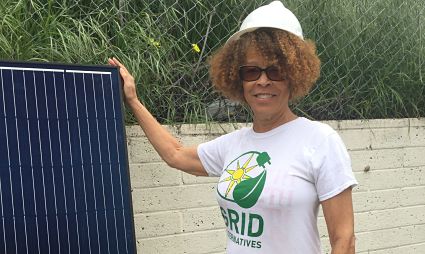 Person holding solar panel wearing GRID Alternatives t-shirt and white cap