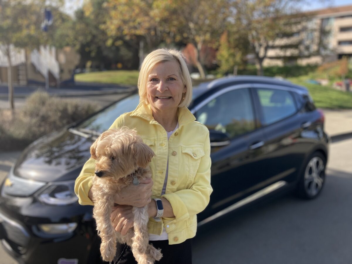 Clean Mobility Program beneficiary is standing next to her recently purchased electric vehicle