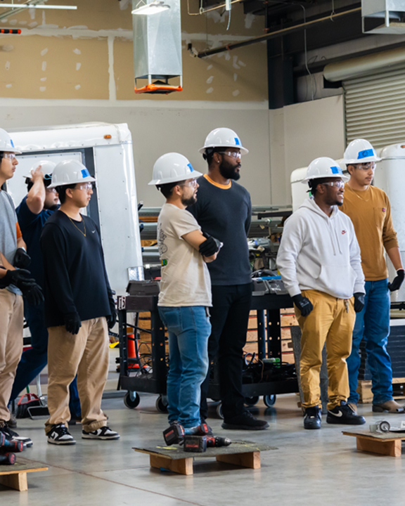 Group of workers wearing hard hats standing in an industrial warehouse facility during a training or tour
