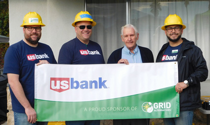 Four people in hard hats holding a US Bank GRID sponsorship banner outdoors
