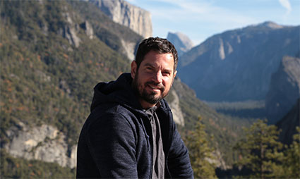 Man smiling at camera with mountain valley and cliffs in background