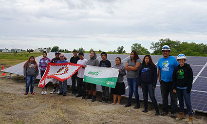 Volunteers next to solar panels holding jinko and tribal signs