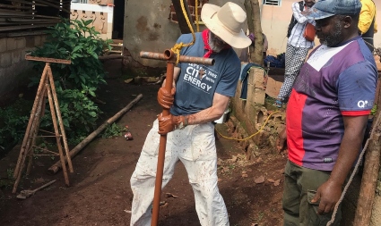 Two men working with soil and tools in a residential outdoor space, one wearing a blue shirt and hat