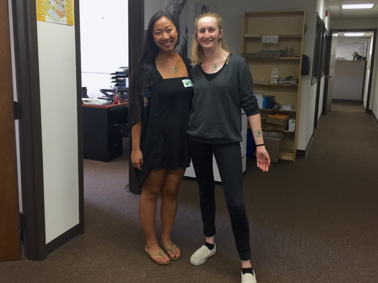 Two smiling women posing together in an office hallway