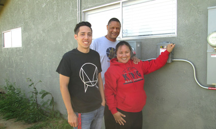 Three people posing together indoors near a window and plants, smiling at camera