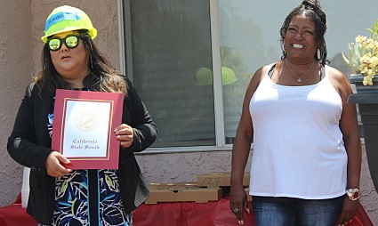 Smiling, a white-shirted homeowner accepts a certificate from another person wearing a safety helmet and dress