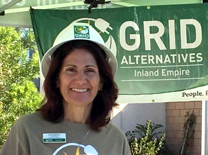 Woman smiling at GRID Alternatives Inland Empire booth wearing hard hat and volunteer shirt