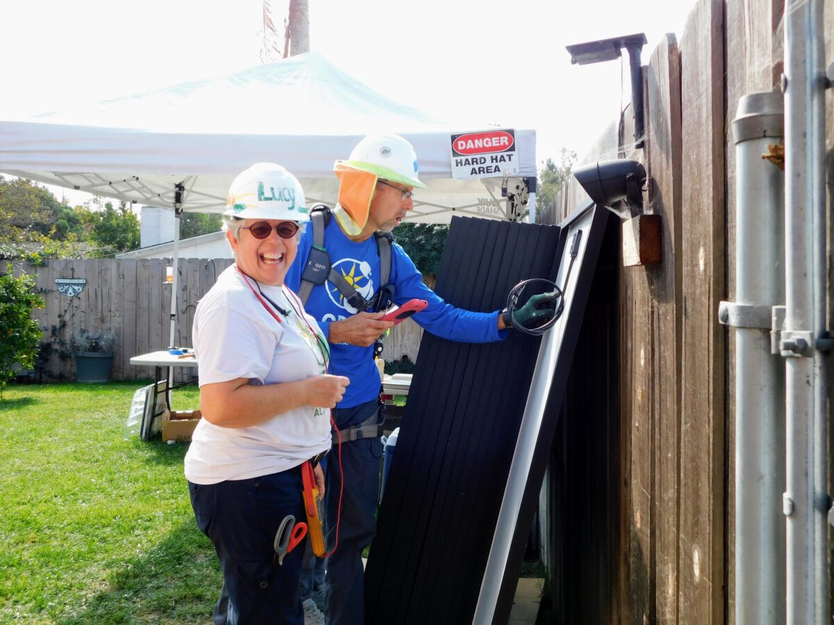Two workers in hard hats and safety gear inspect industrial equipment in a backyard, with a "Danger Hard Hat Area" sign visible