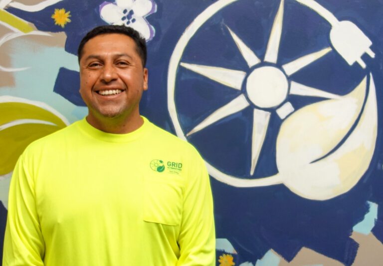 Man in yellow GRID shirt smiling in front of renewable energy mural with wind turbine