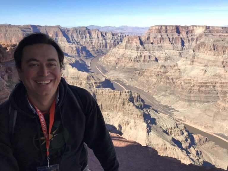 Man smiling at Grand Canyon overlook with river visible below layered rock formations