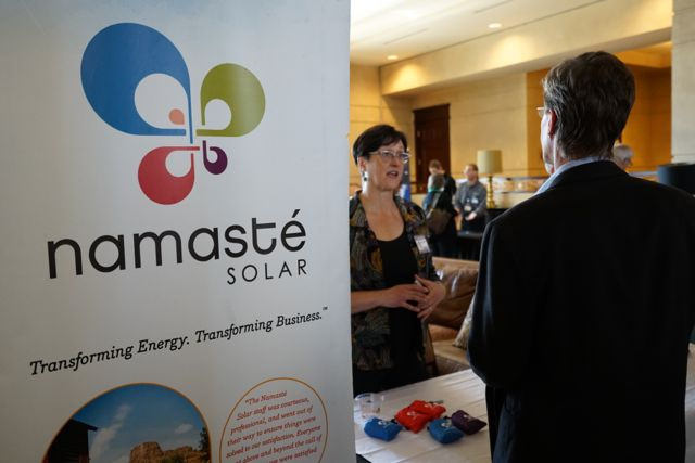 Namaste solar sign says "Transforming Energy. Transforming Business." A woman Namaste recruiter is speaking to a man at Namaste's booth.