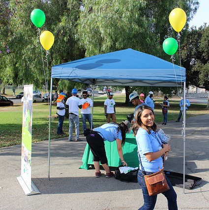 A young person on the GRID Alternatives staff stands in front of an easy-up in a park