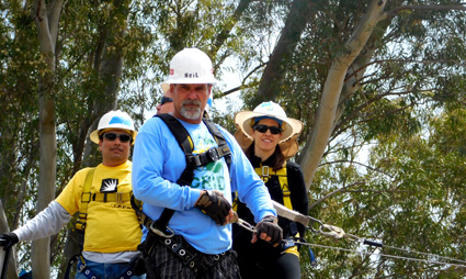 Three people in safety gear on a high ropes course among trees