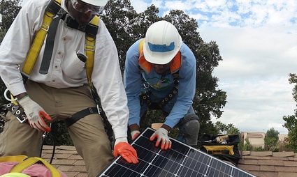 Two workers in safety gear installing a solar panel on a rooftop