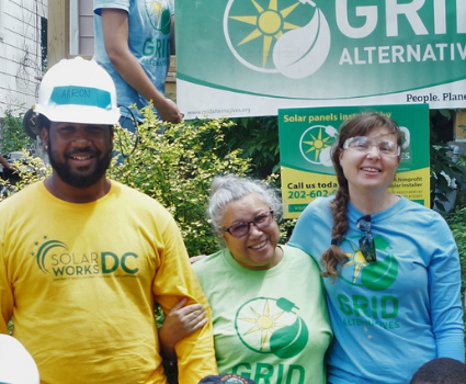 Three people smiling at a solar energy event, wearing green and yellow GRID Alternatives branded clothing