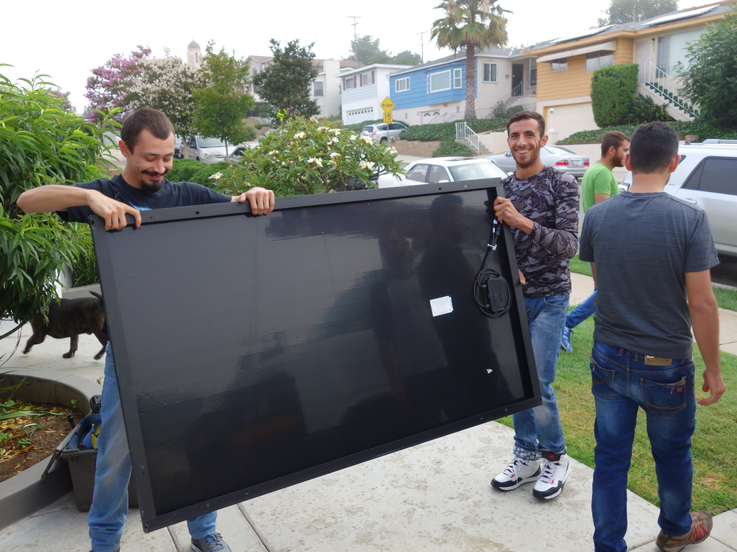 Three refugee volunteers unload solar panels from a GRID van.