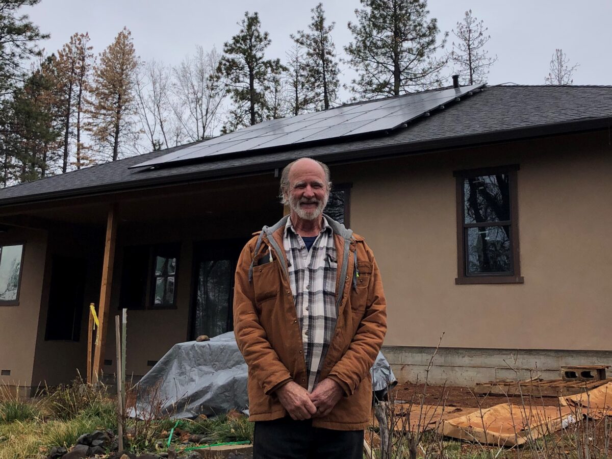 Man standing in front of modern home with solar panels and forest backdrop