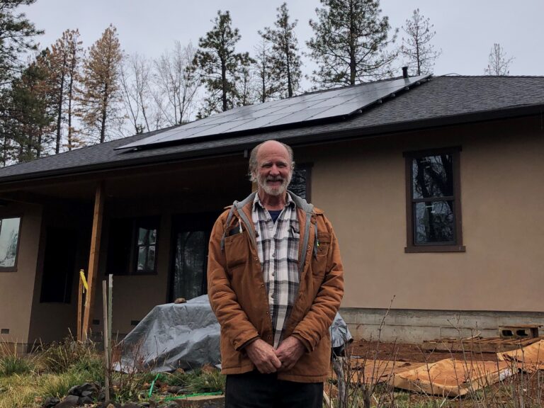 Man standing in front of modern home with solar panels and forest backdrop