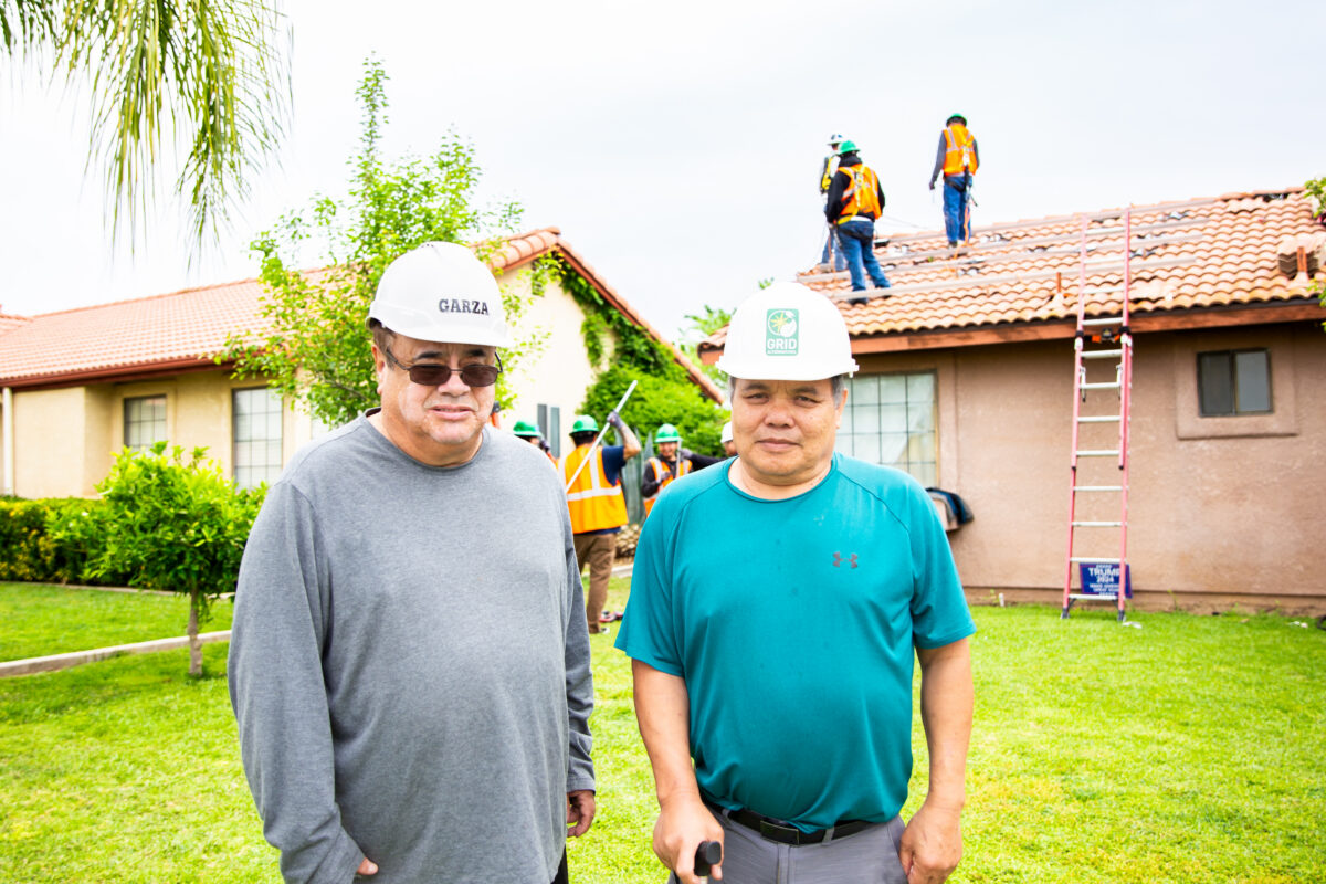 Two men wearing hard hats posing for photo in front of a home
