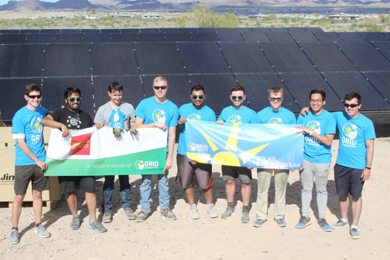 Team in blue GRID shirts holding solar and flags at solar panel installation site