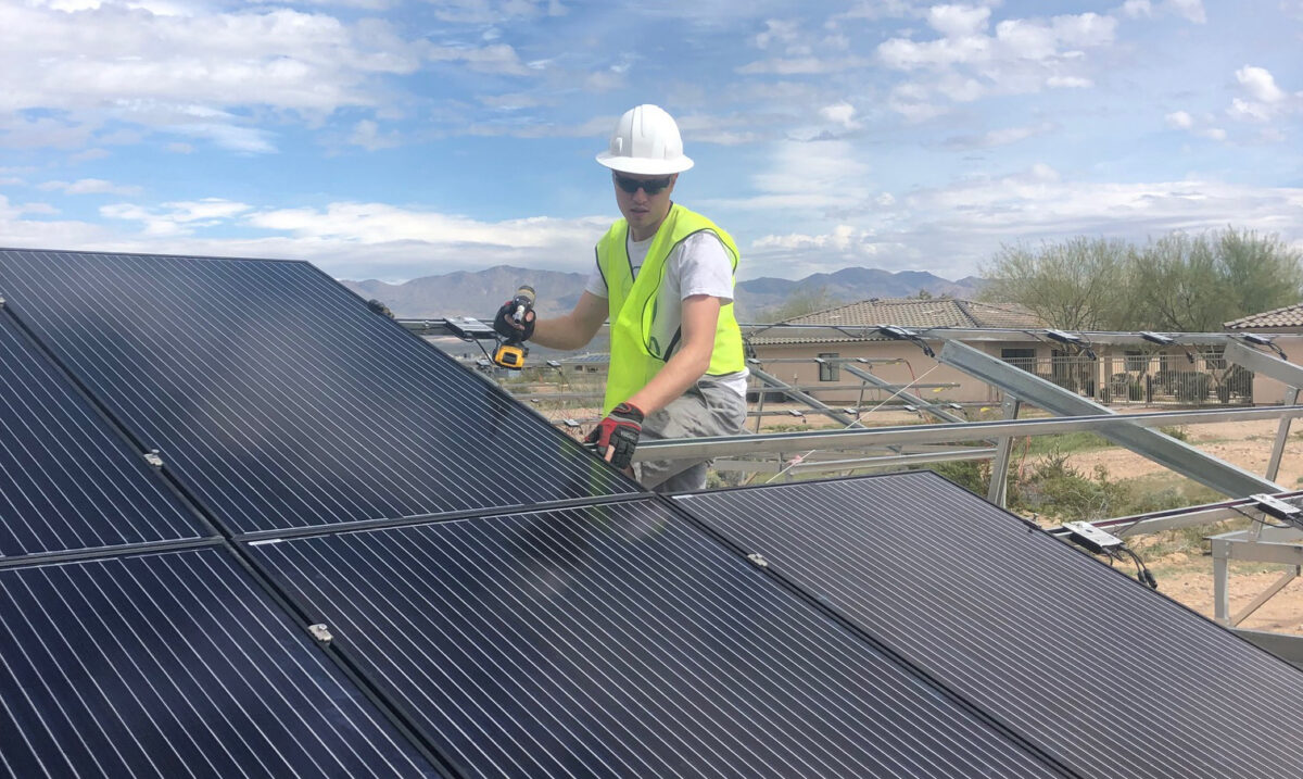 Construction worker installing metal roofing panels on residential building with mountains in background