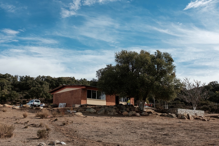 Brick house with red metal roof in arid landscape with scattered trees and boulders