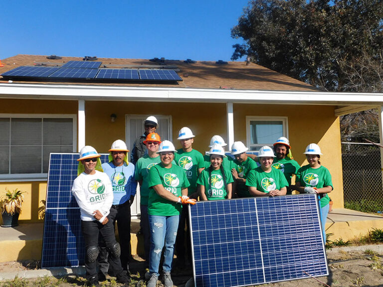 Group of GRID volunteers in green shirts and hard hats with solar panels at a yellow house installation