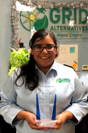 Woman holding award in front of GRID Alternatives Inland Empire office sign