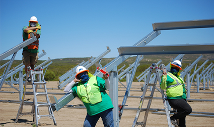 Construction workers in safety gear installing solar panel equipment at a renewable energy site