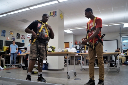 Two high school students demonstrate how to correctly wear a safety harness during a class presentation.