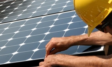 Worker in yellow hard hat installing solar panel on rooftop