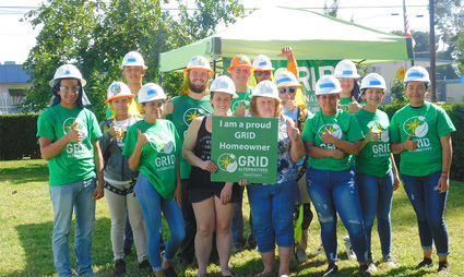 Group of volunteers in green GRID shirts and hard hats holding a sign at an outdoor event