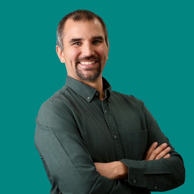 Smiling man with beard wearing dark teal button-up shirt against teal background