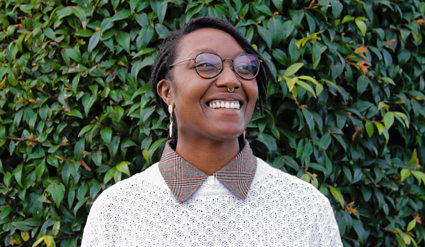 Smiling person wearing glasses and patterned shirt against ivy-covered wall