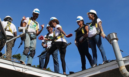 Group of workers in hard hats and safety vests standing on a metal roof structure against blue sky